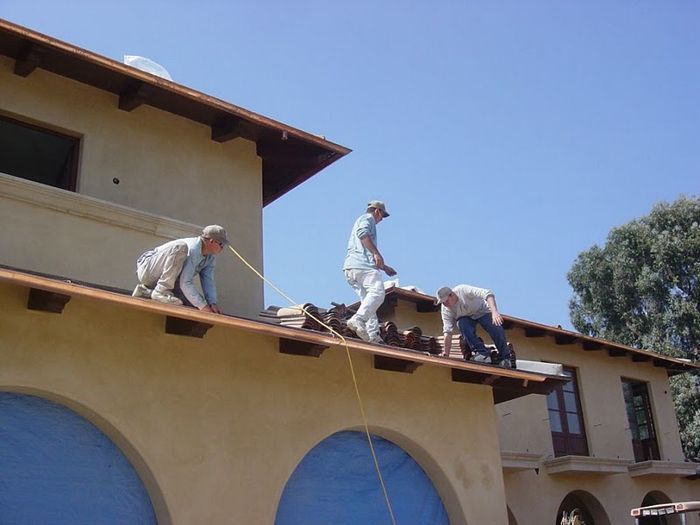 Three roofers working on a brown tiled roof on a sunny day.