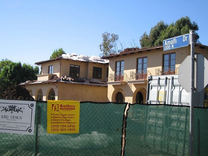 House under construction, behind a green fence, corner of Armati Dr. Street sign is visible.
