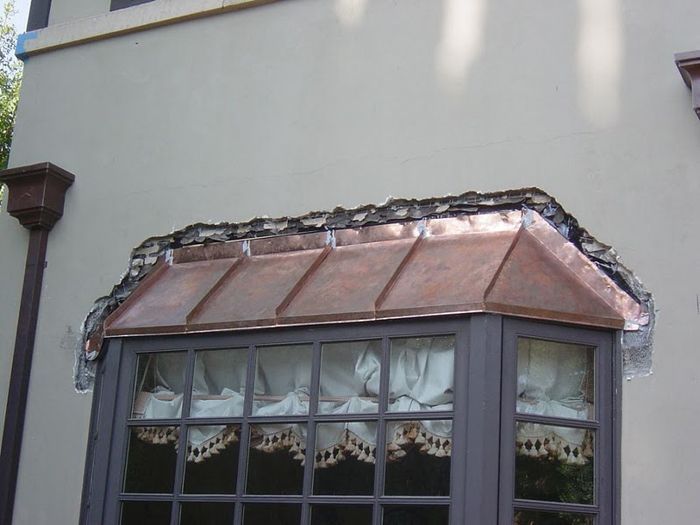 Copper window overhang on a beige wall. Dark window frame with light curtains.