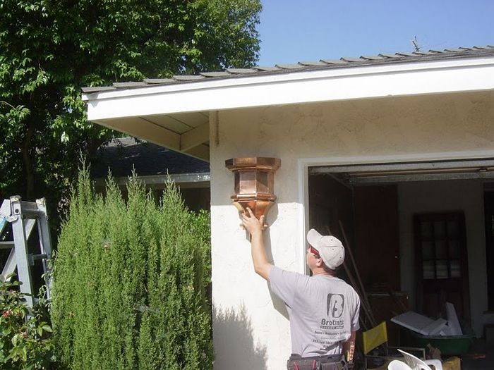 Man installing a brown lantern on a stucco building near a garage.