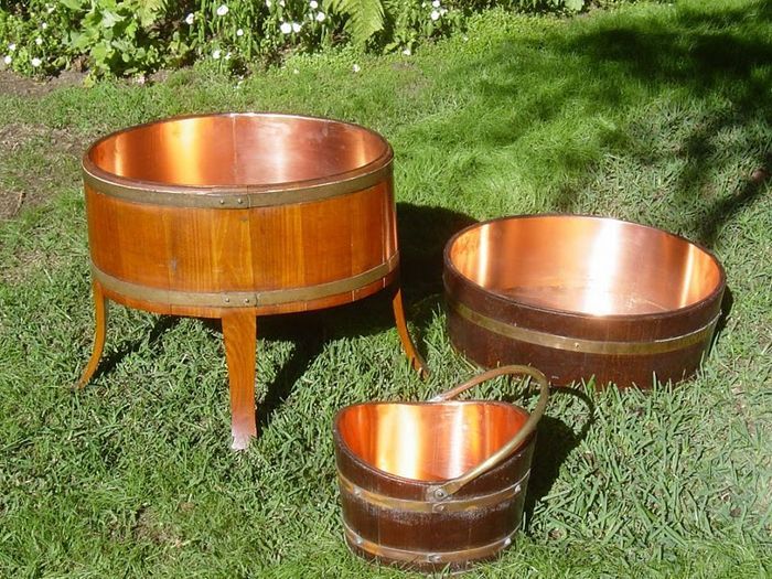 Three wooden and copper tubs on green grass.