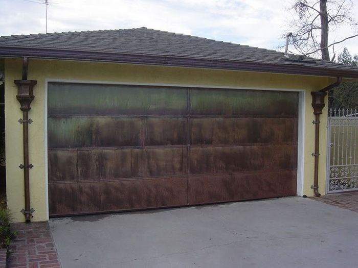 Brown garage door on a yellow building with copper accents. Concrete driveway in front.