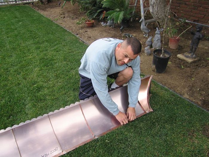 Man kneeling on grass, attaching copper sheet. Backyard setting.