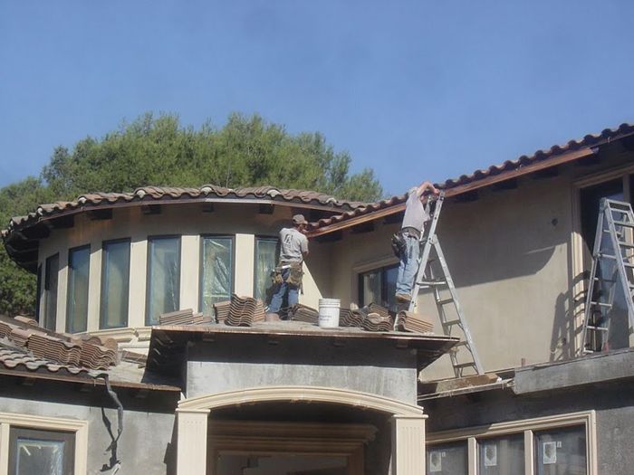 Two roofers working on a house with curved walls and tiled roof on a sunny day.