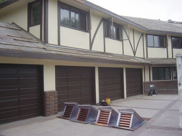 Row of brown garage doors under a Tudor-style building. Several solar vent boxes are in the driveway.
