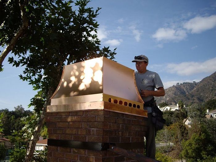 Man installing a copper chimney cap on a brick chimney. Bright sunlight.