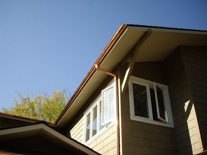 Brown house with copper gutters and white-framed windows against a blue sky.