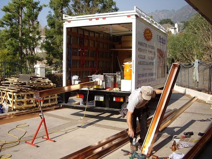 Man using a power drill near an open moving truck, likely working on lumber, in a driveway.
