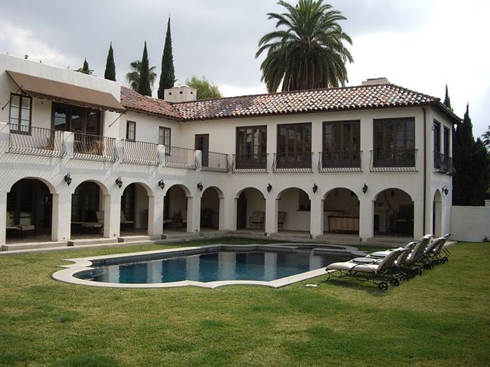 Backyard view of a large white stucco house with a pool and lawn.