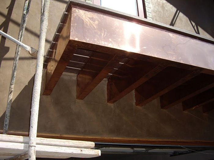 Copper-colored metal awning with a sawtooth design, attached to a brown wall, scaffolding visible.