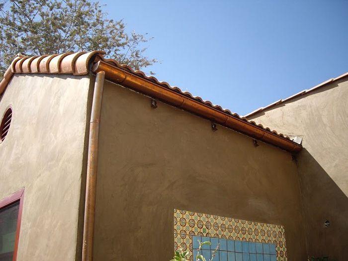Tan stucco building with brown trim, clay tile roof, and decorative tiles.