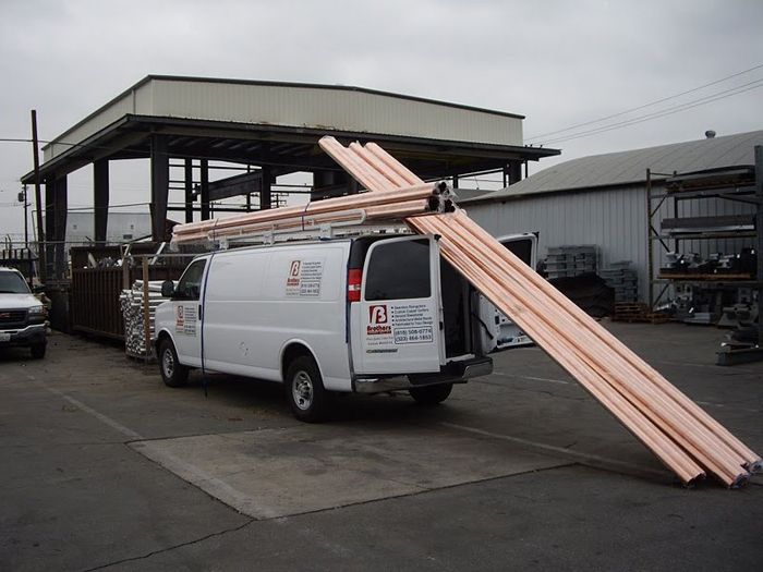 White work van loaded with copper pipes, parked in an industrial area.