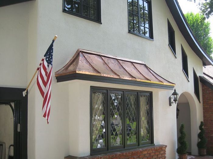 Two-story house with a copper awning over a window, an American flag, and a brick base.