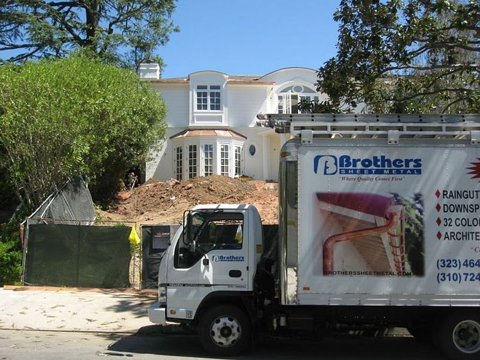 White truck parked in front of a white house under construction; earthworks in front, trees on sides.