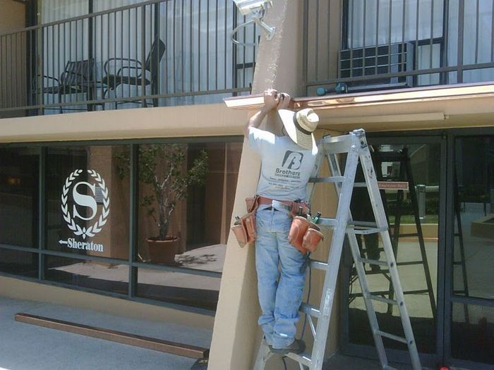 Man on ladder installing wood trim at Sheraton hotel entrance.