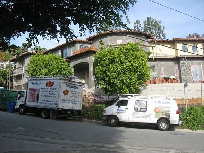 Construction vehicles parked on street in front of a building under construction with stucco walls.