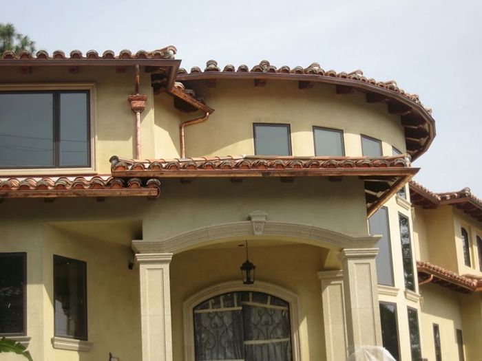 Beige stucco house with brown tile roof, arched entryway, and dark-framed windows.