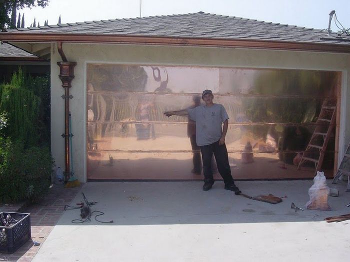 Man pointing at a copper garage door on a house. He stands in front of the garage.