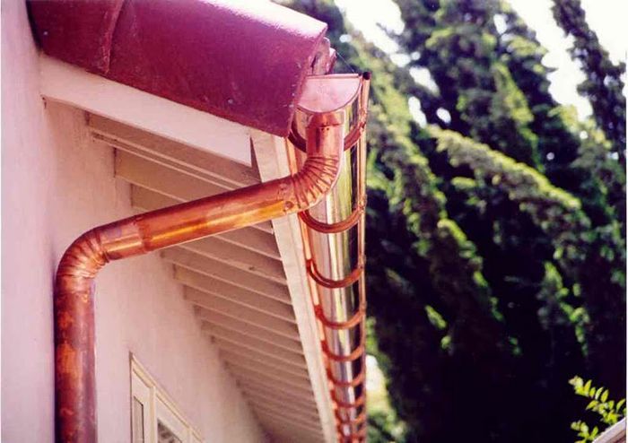 Copper rain gutters on a building's edge with a natural backdrop.