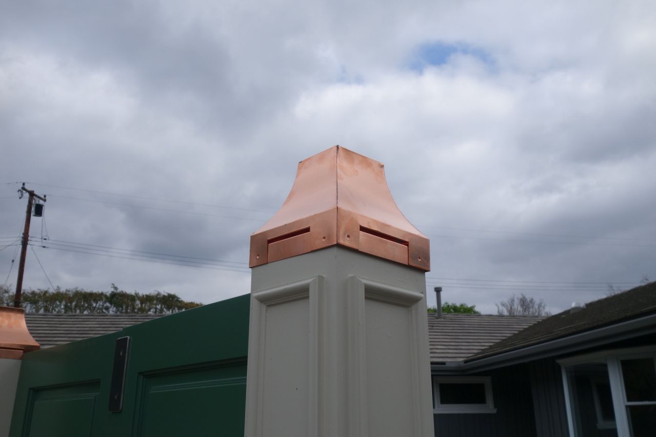 Copper-capped cream-colored column on a green gate under a cloudy sky.