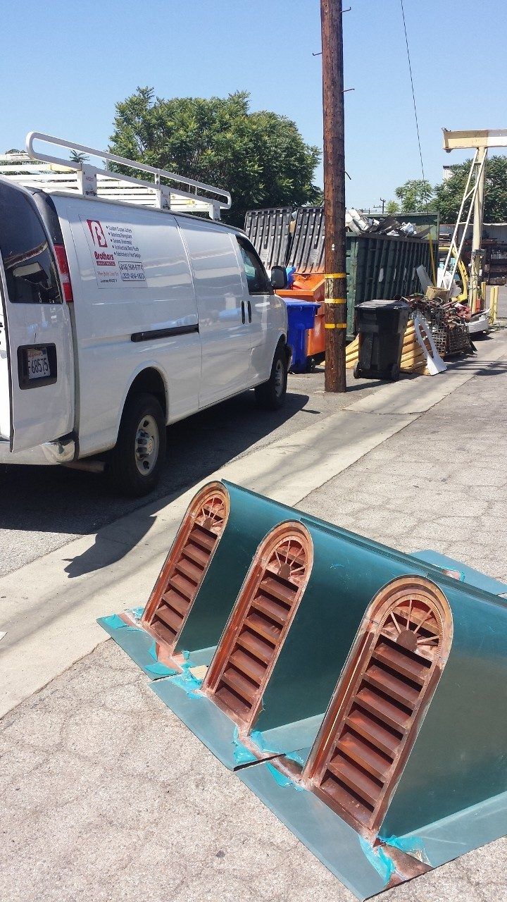 White van parked next to a curb, with metal vents in the foreground. Outdoor setting, sunny day.