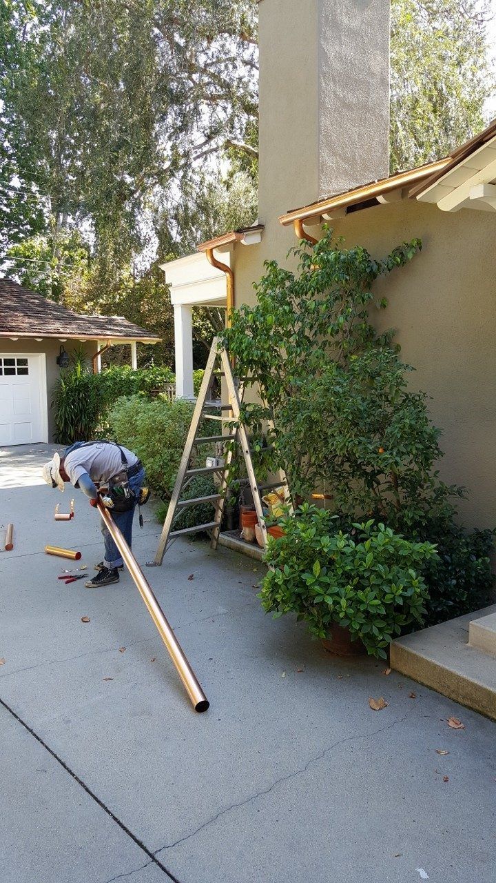 A construction worker uses tools near a house, a ladder, and a tree on a driveway.