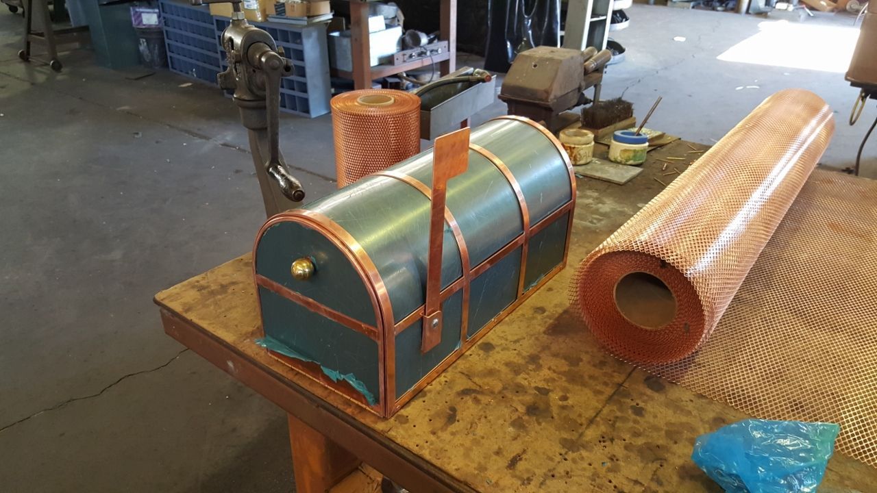 Copper mailbox with copper trim, sitting on a wooden table. Rolls of copper mesh are nearby.