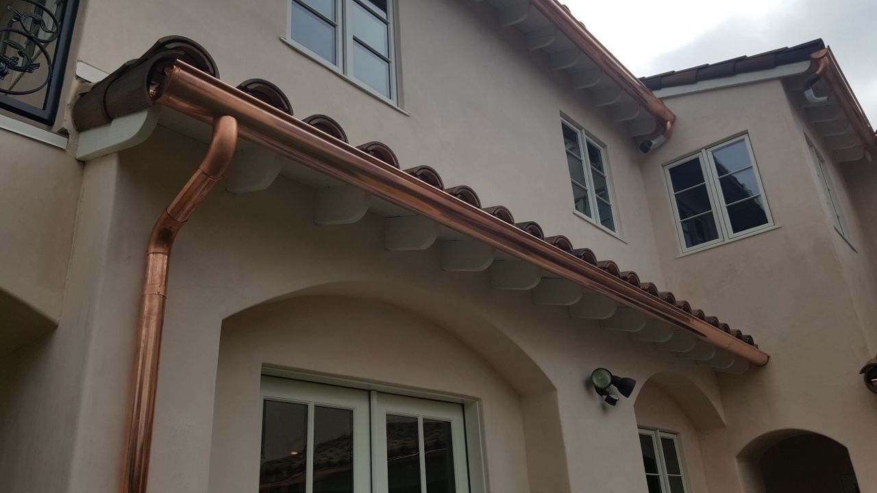 Copper gutters on a light-colored stucco building with red tile roof.