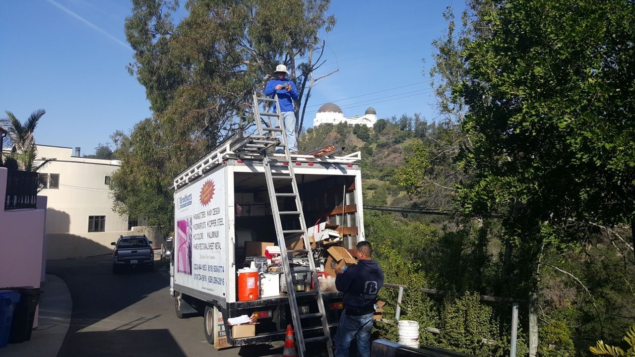 Movers loading truck, one on roof, next to Griffith Observatory, on a sunny day.