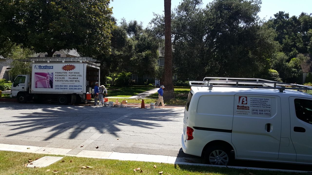 A moving truck and a van parked on a street; people are transferring items; sunny day.