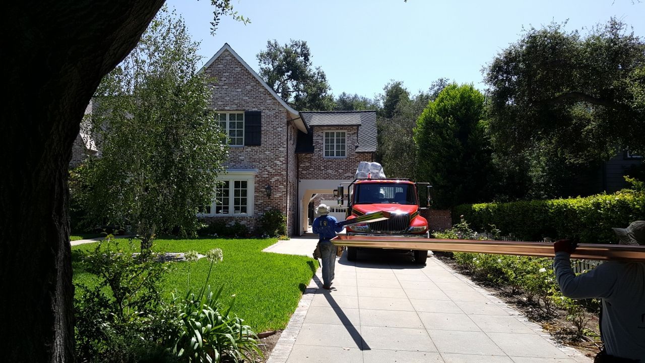 Two workers carrying lumber toward a brick home, red truck in driveway.