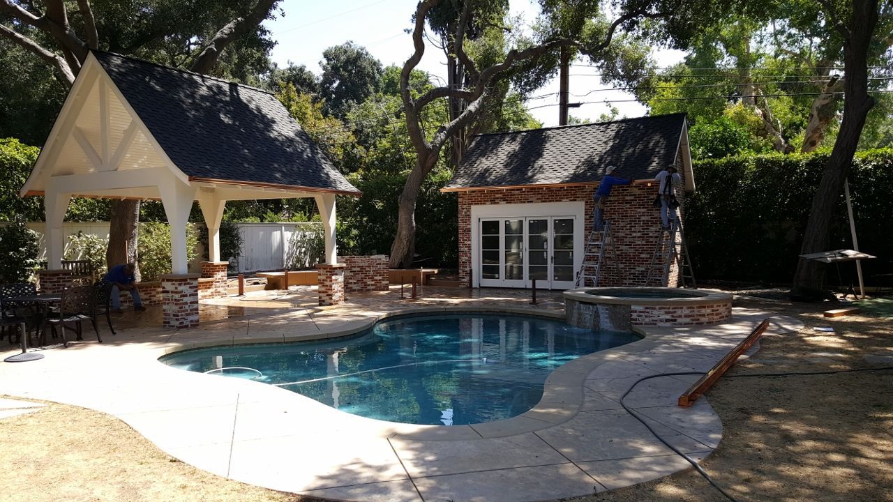 Pool with a gazebo and small building, all under construction in a backyard.