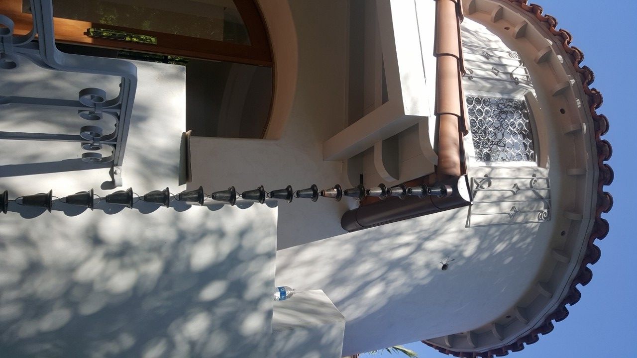 Corner of a round building with a rain chain, brown gutter, and terra cotta roof tiles.