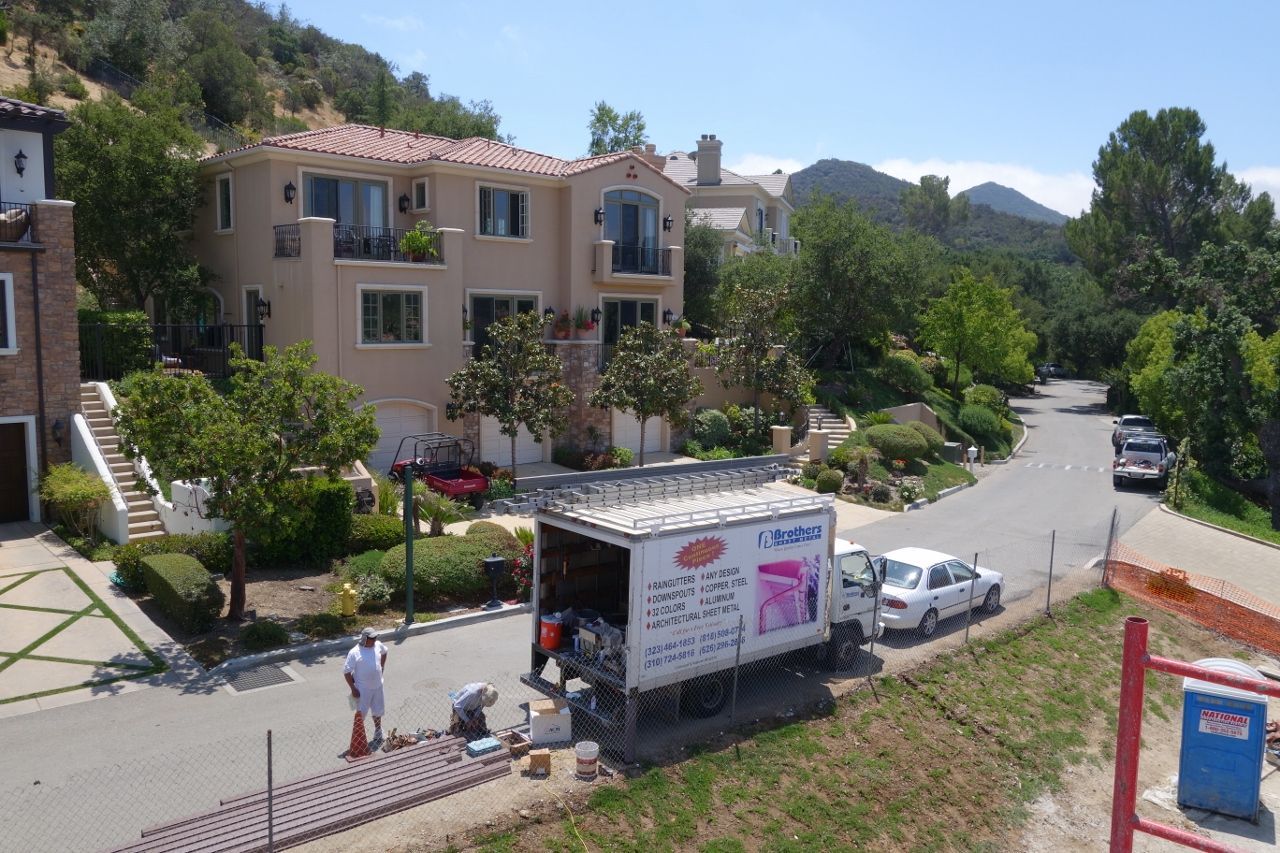 Moving truck parked in front of a large beige house on a sunny street; workers nearby.
