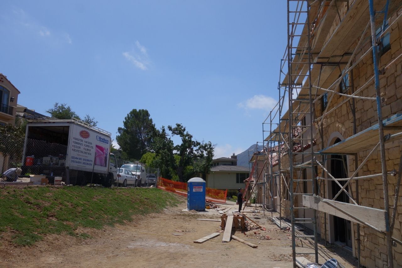 Construction site with scaffolding on a building, a work truck, portable toilet, and debris.