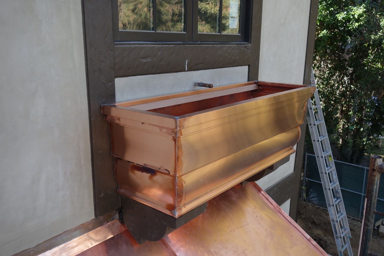 Copper planter box mounted under a window, with copper accents on a building exterior.
