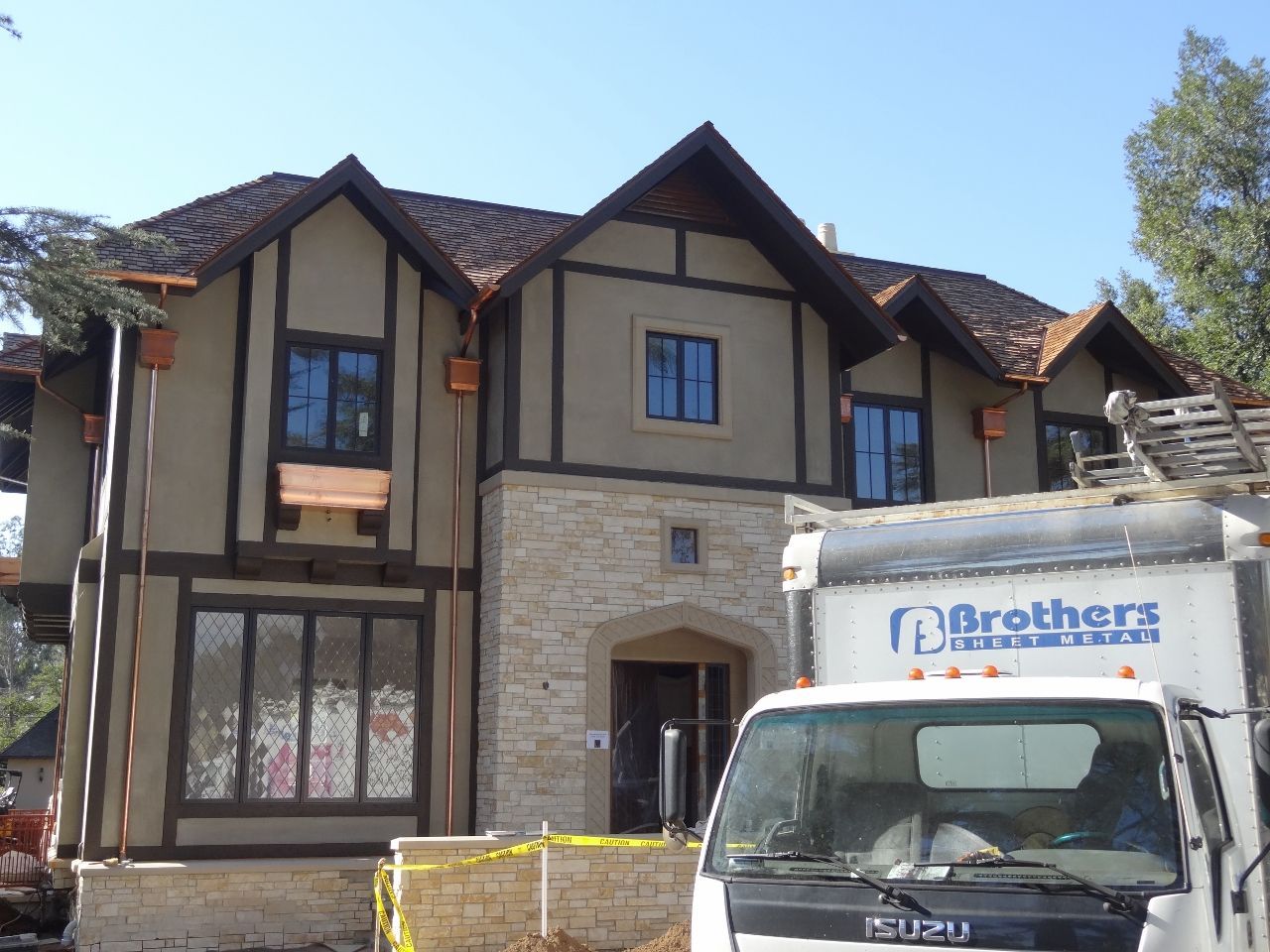 Two-story Tudor home under construction, with stucco, brown trim, and stone accents. A truck is parked in front.