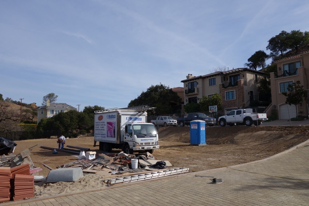 Construction site with a truck, portable toilet, debris, and buildings in the background.