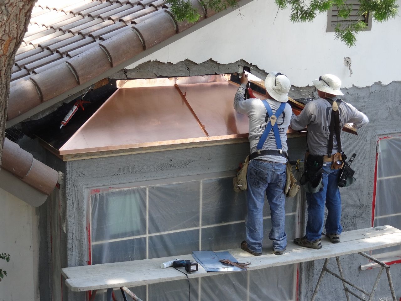 Two construction workers install copper roofing on a building.
