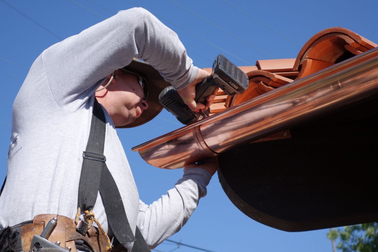 Man installing copper gutter with a power drill on a sunny day.
