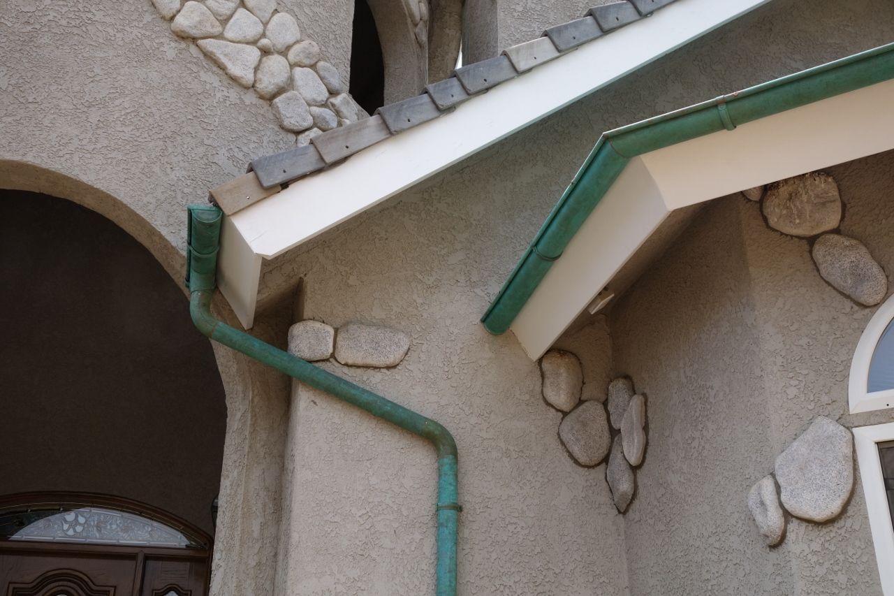 Green gutters on a stucco house with stone accents.