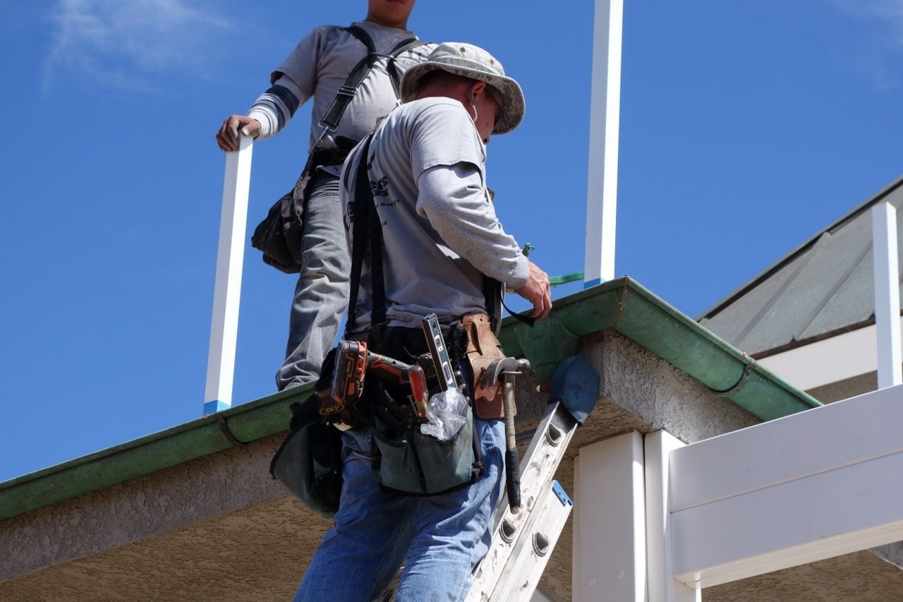 Two construction workers installing a railing on a building. Blue sky.