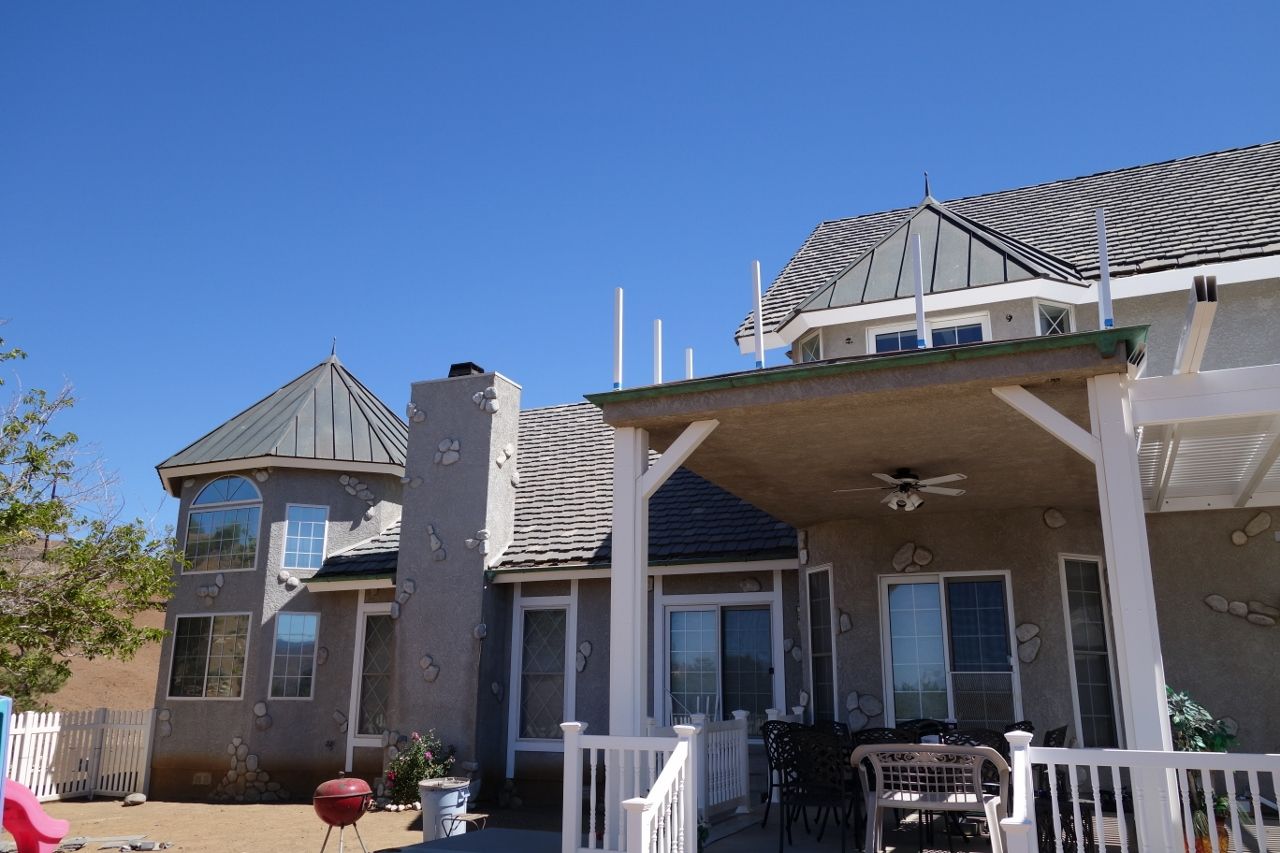 House with unique roof designs under a clear blue sky, featuring a patio and fenced backyard.