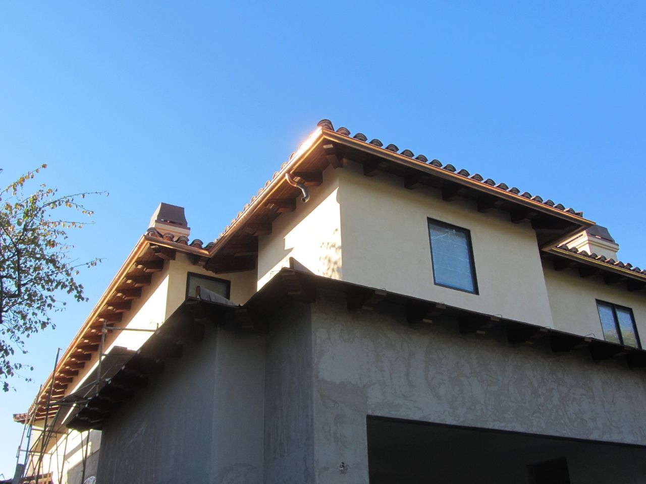 Beige two-story stucco house with a brown tile roof, copper gutters, and a blue sky.
