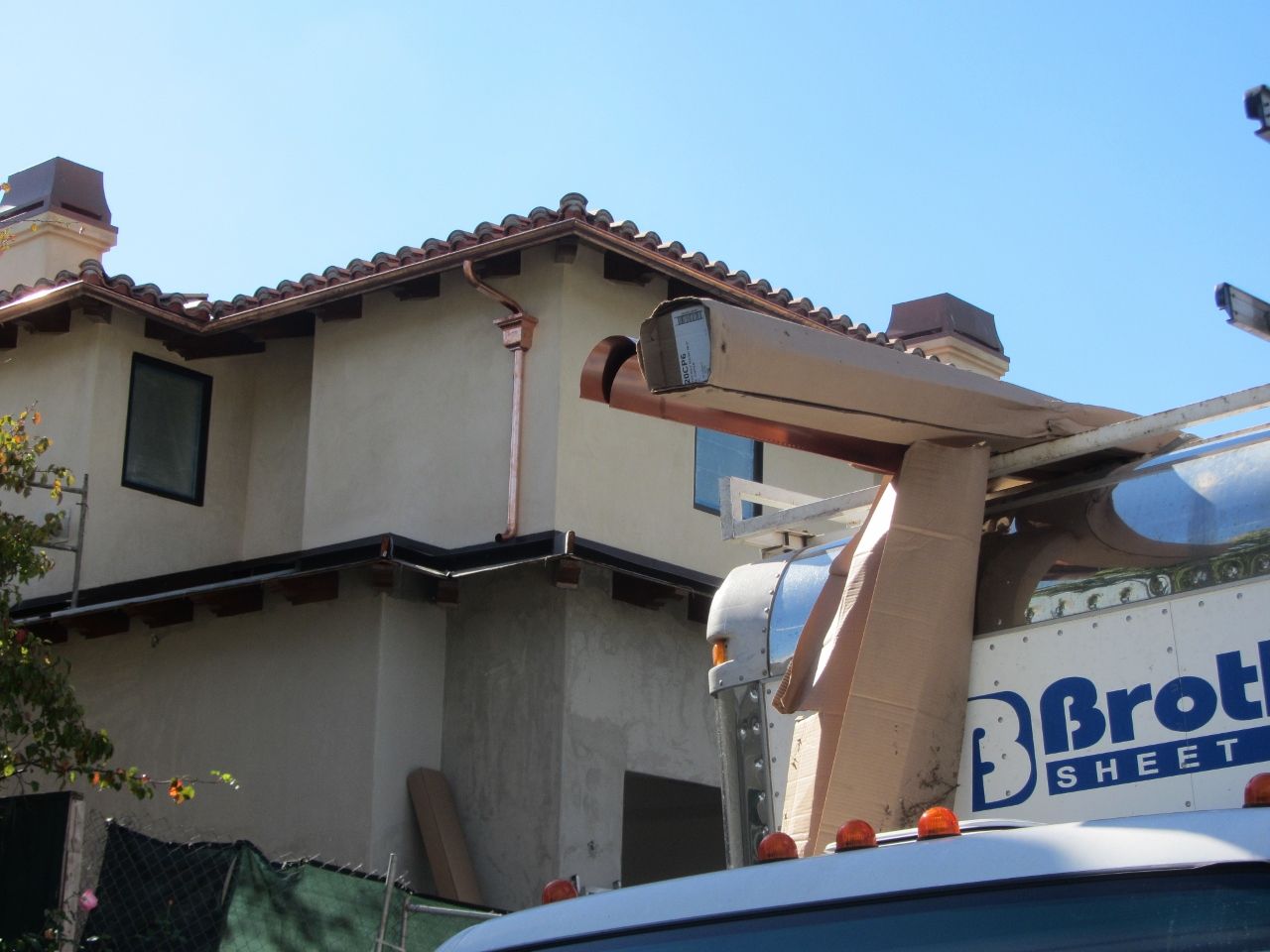 Two-story beige stucco house with copper gutters; a utility truck is in front.