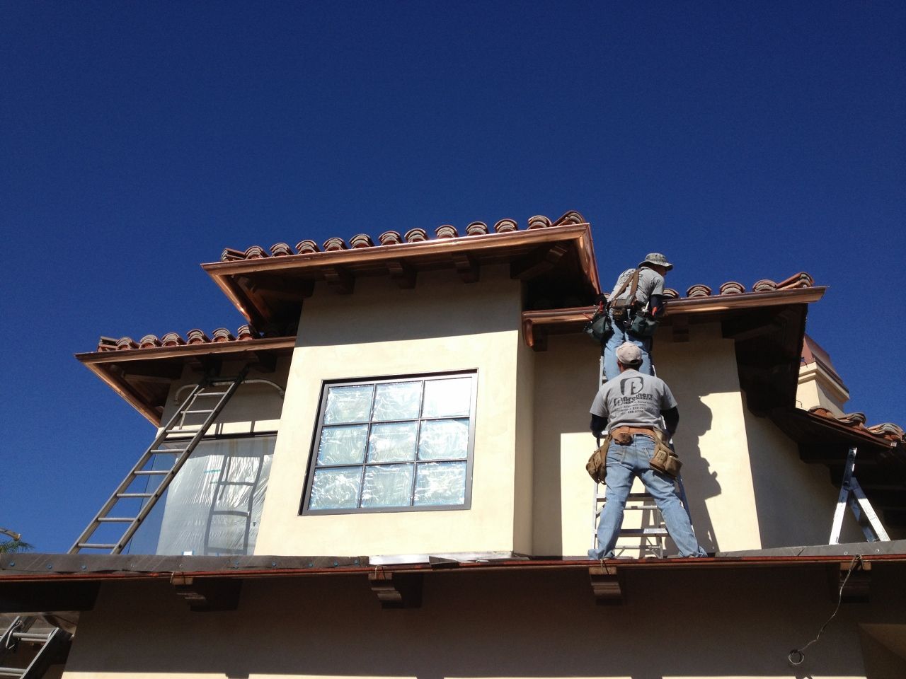 Two construction workers on a rooftop, installing copper gutters against a bright blue sky.