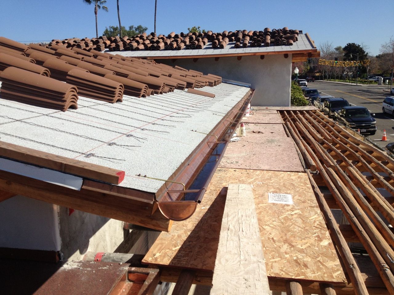 Roof under construction with brown tiles, a copper gutter, and exposed wooden beams.