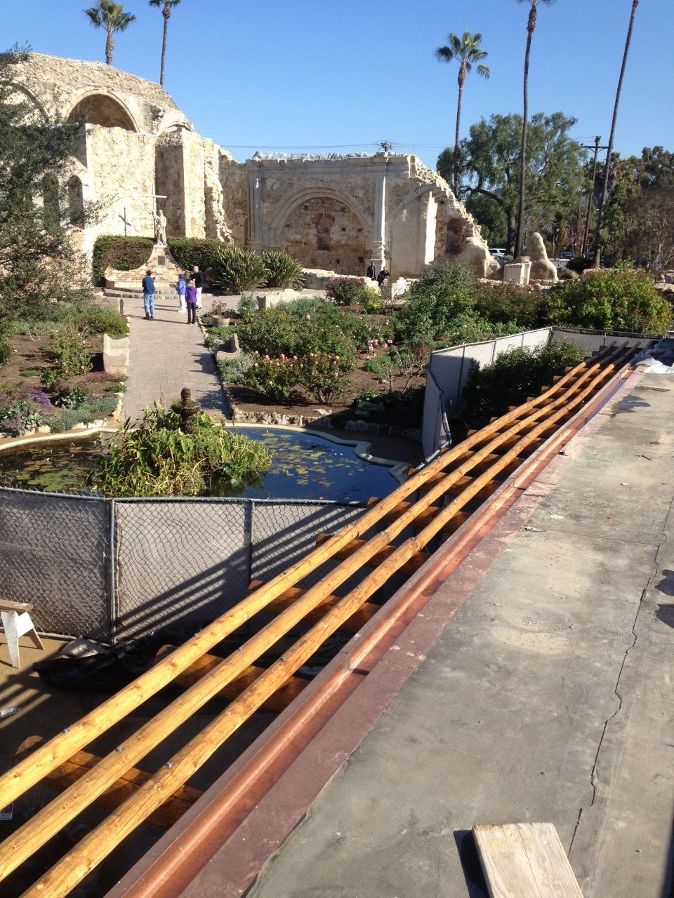 View of Mission San Juan Capistrano with a set of wooden poles and garden.