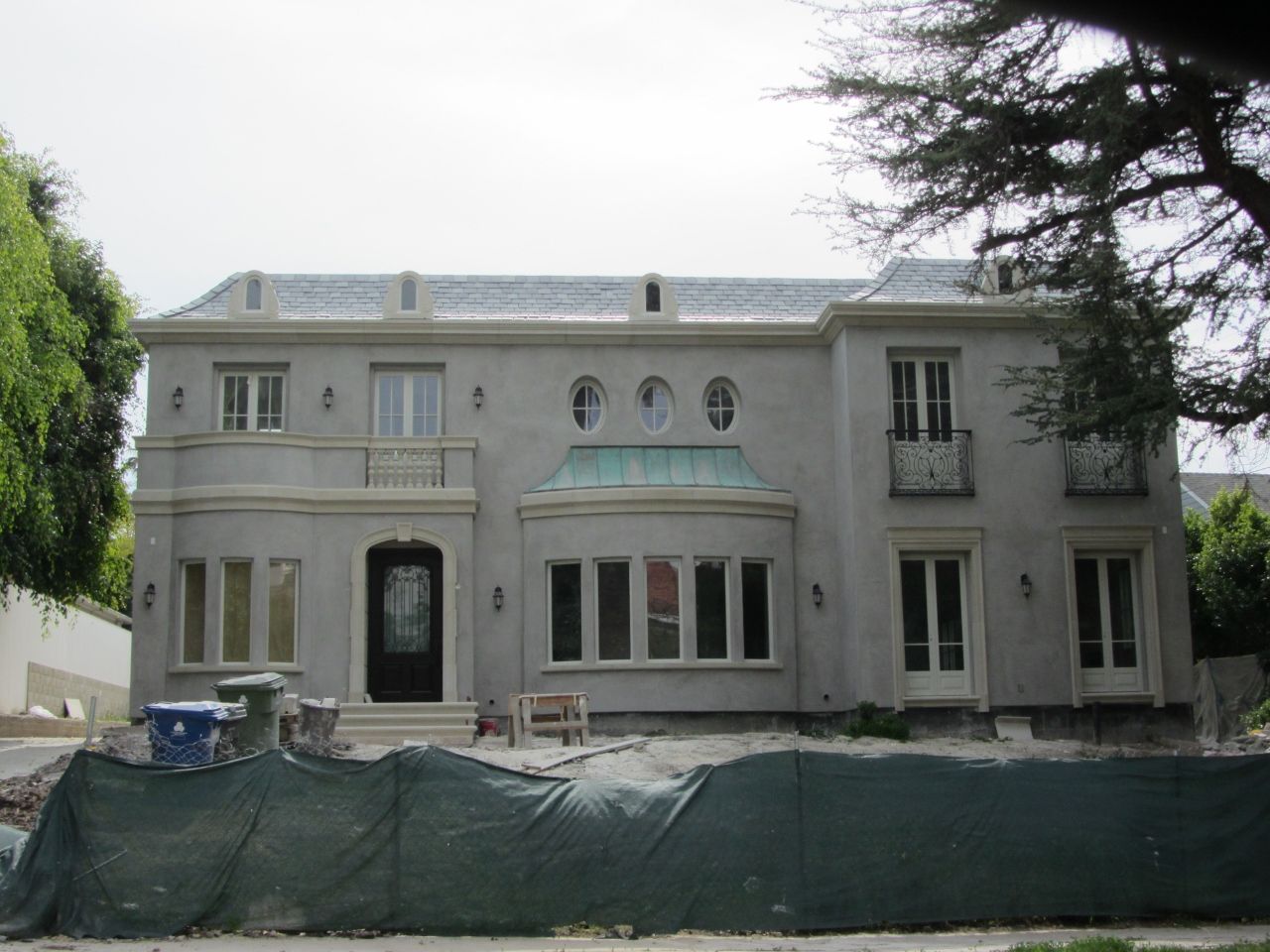 Gray stucco house under construction with a green tarp in front.