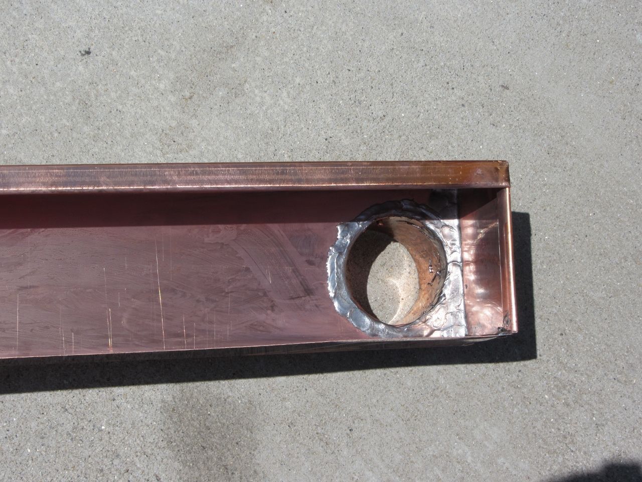 Copper channel with a circular hole cut in the side, likely for a pipe fitting.